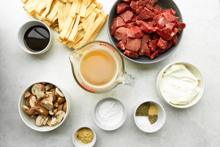 Photo of all the ingredients for Slow Cooker Beef Stroganoff including raw beef, beef broth, mushrooms, seasonings, Worcestershire sauce