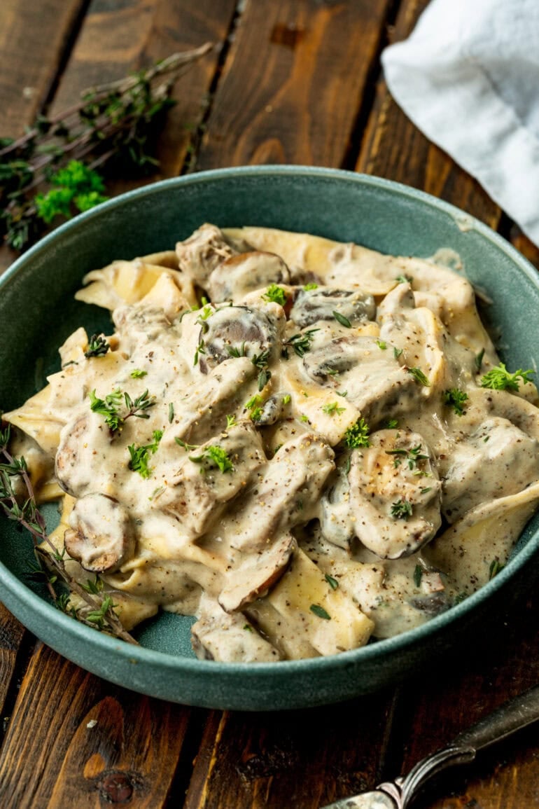 Photo of a bowl of beef stroganoff mixed with cooked egg noodles, mushrooms and fresh herbs
