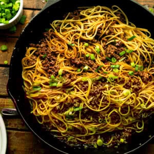 a photo of a cast iron skillet full of cooked spaghetti noodles tossed with ground beef and chopped scallions