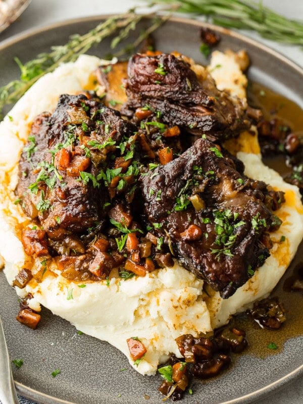A dark grey plate with a pile of creamy mashed potatoes with fall apart braised beef short ribs and fresh parsley