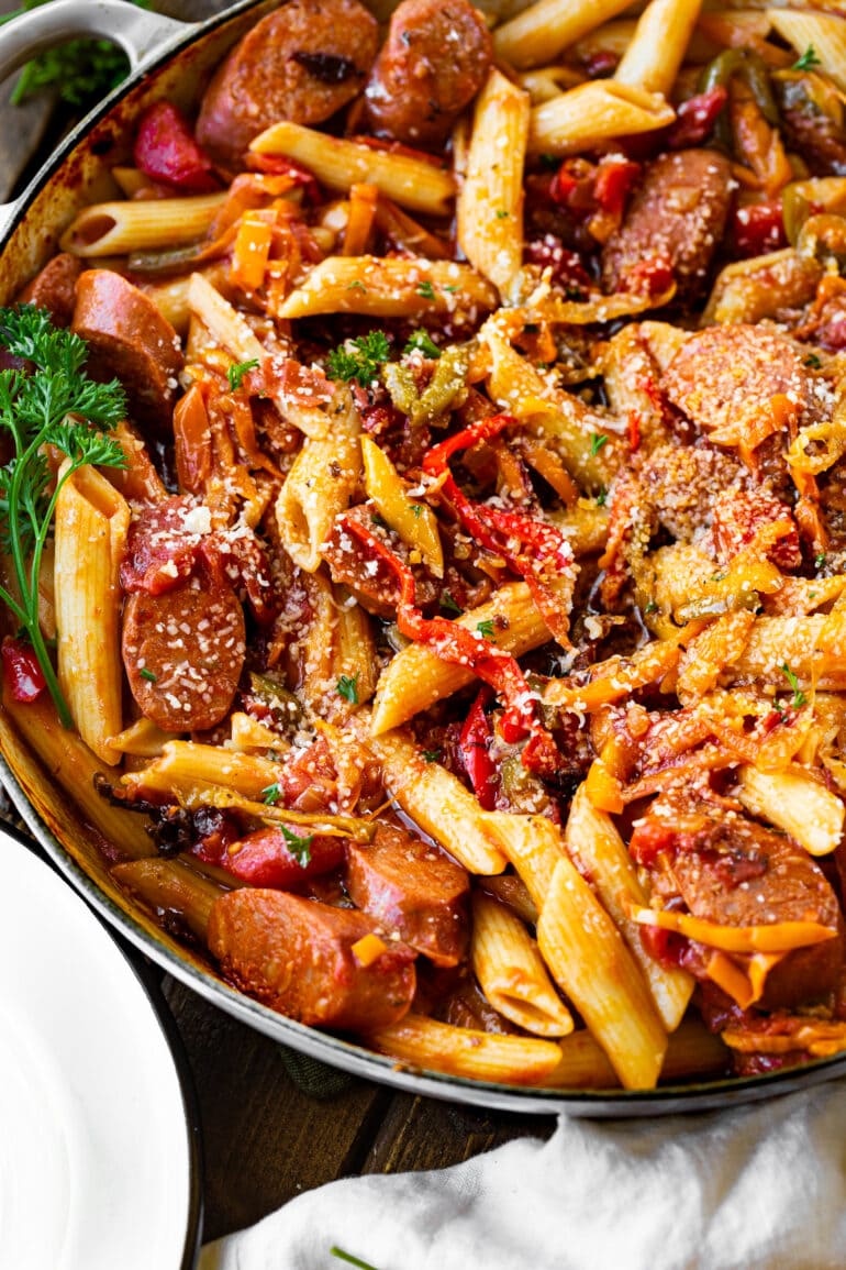a photo of cooked penne pasta in a skillet mixed with sauteed peppers and onions and sausage.