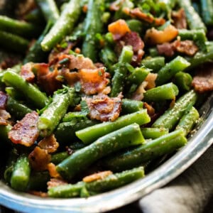 A silver serving dish with bright green beans that have been chopped and served with crumbled bacon ohsweetbasil.com
