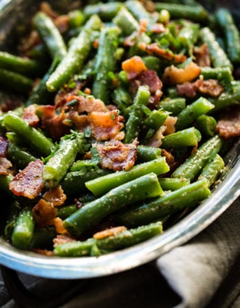 A silver serving dish with bright green beans that have been chopped and served with crumbled bacon ohsweetbasil.com