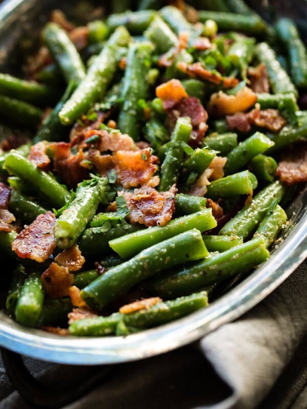 A silver serving dish with bright green beans that have been chopped and served with crumbled bacon ohsweetbasil.com