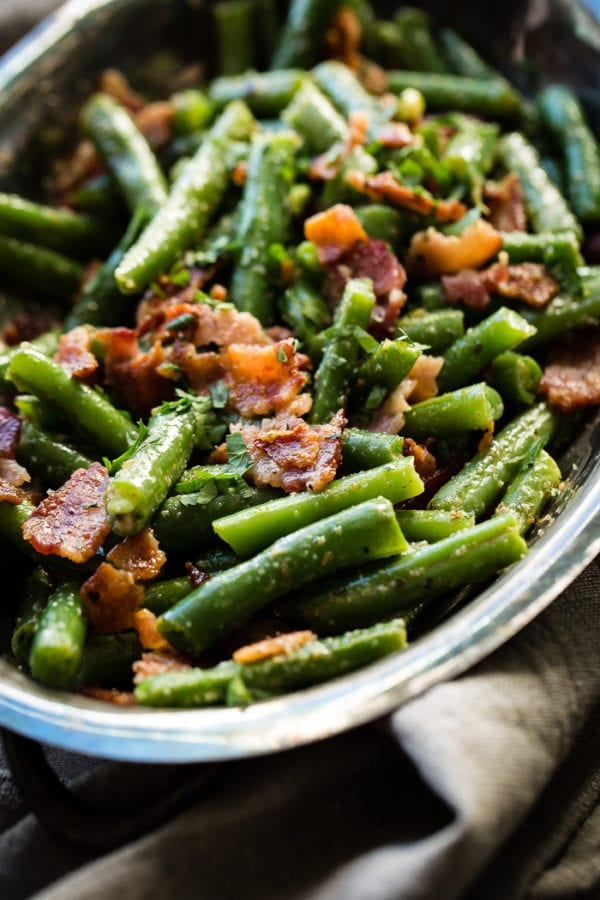 A silver serving dish with bright green beans that have been chopped and served with crumbled bacon ohsweetbasil.com