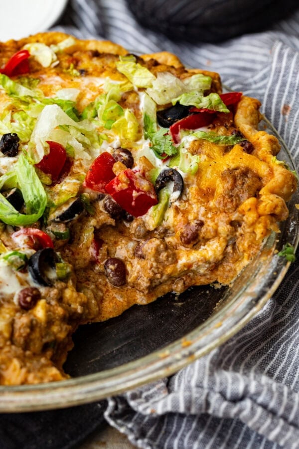 a photo of a pie tin full of taco pie - ground beef, melted cheese, shredded lettuce, tomatoes, sour cream and black olives on top