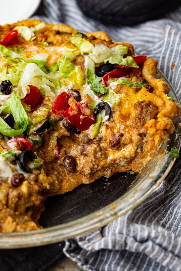 a photo of a pie tin full of taco pie - ground beef, melted cheese, shredded lettuce, tomatoes, sour cream and black olives on top