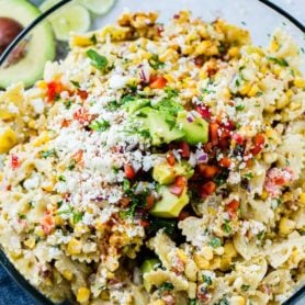 A close up photo of a bow tie pasta salad with avocados, peppers, grilled corn, cilantro, and cotija cheese making up an Elote Mexican Corn Pasta Salad