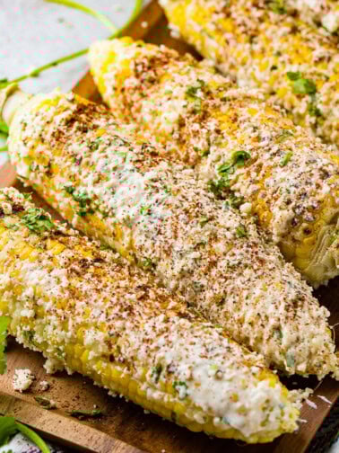 A photo of several cobs of elote mexican street corn lathered in cotija cheese and seasonings.