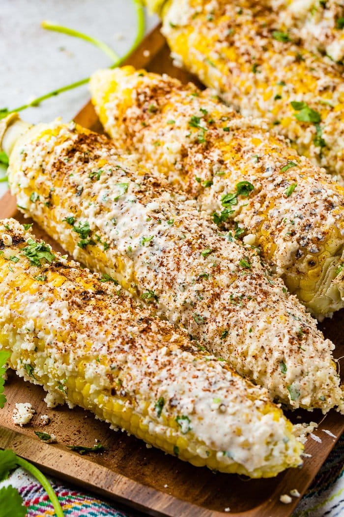 A photo of several cobs of elote mexican street corn lathered in cotija cheese and seasonings.