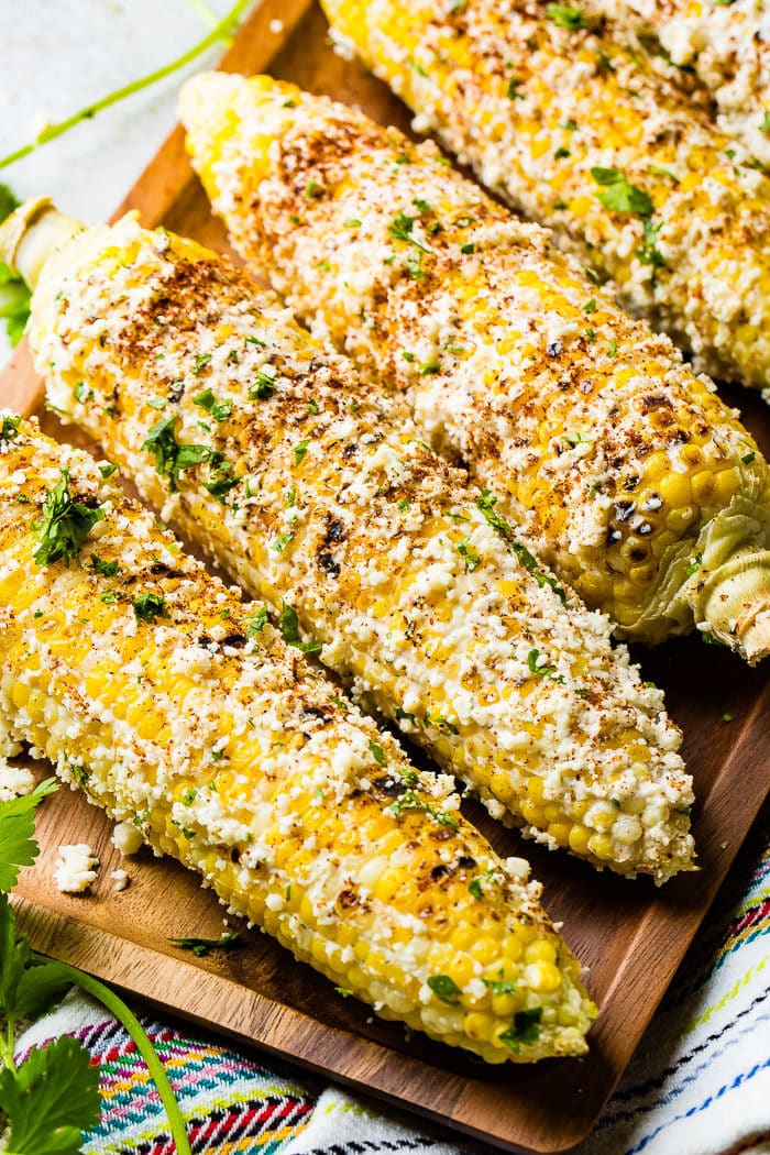 A photo of several cobs of elote mexican street corn lathered in cotija cheese and seasonings.