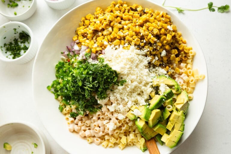cooked pasta being stired with charred corn, cilantro, cotija cheese, avocado and a creamy dressing