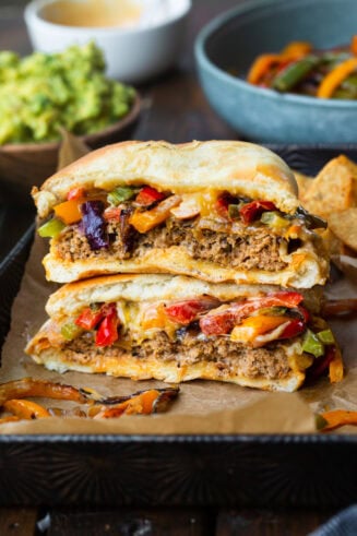 a photo of a mexican fajita burger that has been cut in half and stacked on top of each other so you can see the inside of the burger topped with onions and peppers
