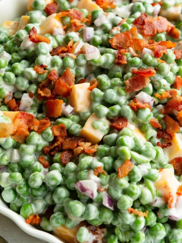 a large bowl of creamy english pea salad topped with crispy bacon bits and cubes of cheddar cheese
