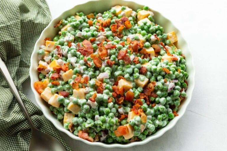 a large bowl of creamy pea salad topped with crispy bacon bits