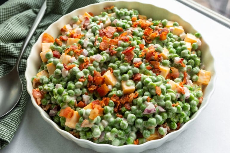 a large white serving bowl of creamy English pea salad
