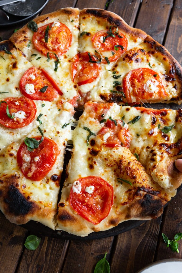 a photo of a four cheese margherita pizza that has been sliced with two of slices pulled out from the rest of the pizza a little bit.