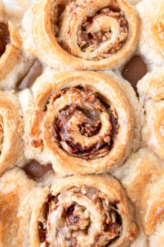 a photo taken over the top of a pan of golden baked apple cinnamon rolls topped with a sweet glaze
