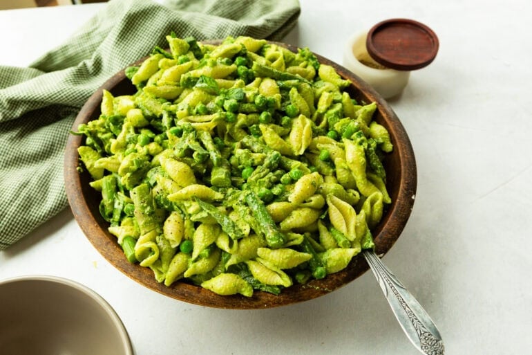A close up of A large wooden bowl filled with green goddess pasta salad with a spoon