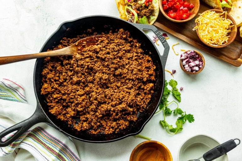 a large cast iron skillet full of cooked seasoned ground beef with a wooden spoon stirring it