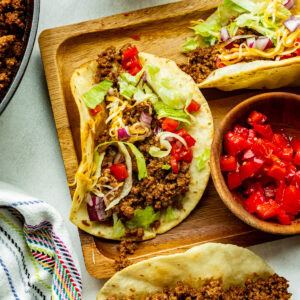 a wooden board topped with ground beef tacos in corn tortillas