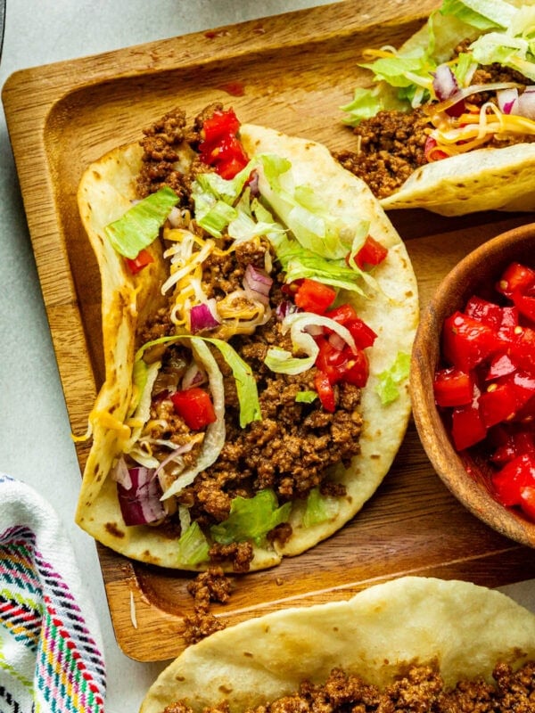 a wooden board topped with ground beef tacos in corn tortillas