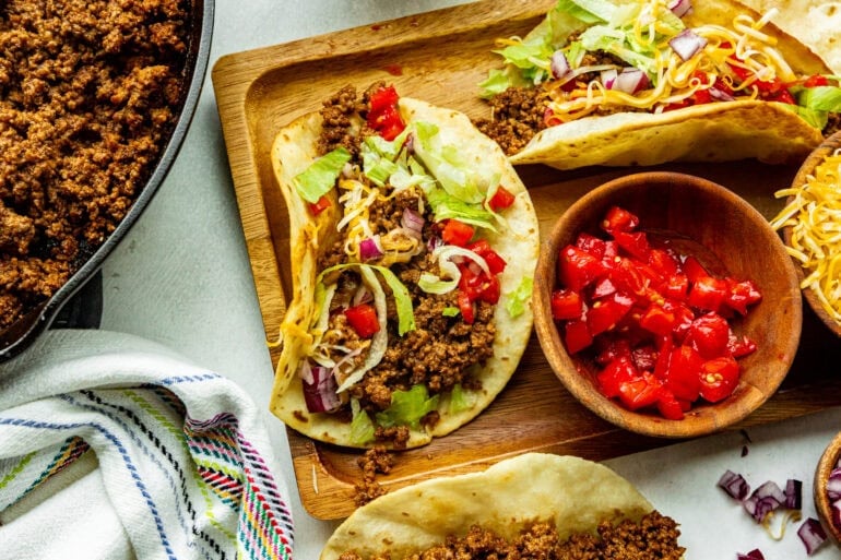 a wooden board topped with ground beef tacos in corn tortillas