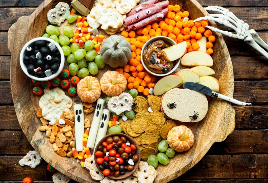 a large circular wooden charcuterie board filled with halloween themed snacks