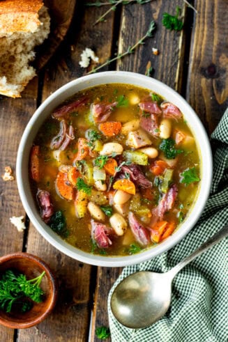 a photo of a large bowl of ham and bean soup with a large chunk of crusty bread next to it and a spoon