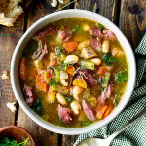 a photo of a large bowl of ham and bean soup with a large chunk of crusty bread next to it and a spoon