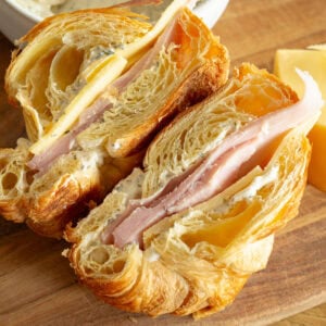 a ham and cheese sandwich on a flaky croissant that has been sliced in half so you can see the inside of each half