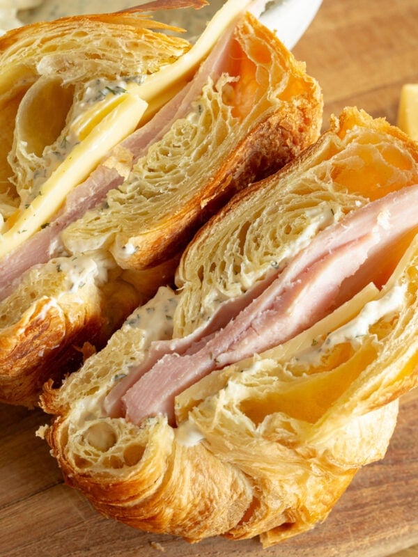 a ham and cheese sandwich on a flaky croissant that has been sliced in half so you can see the inside of each half
