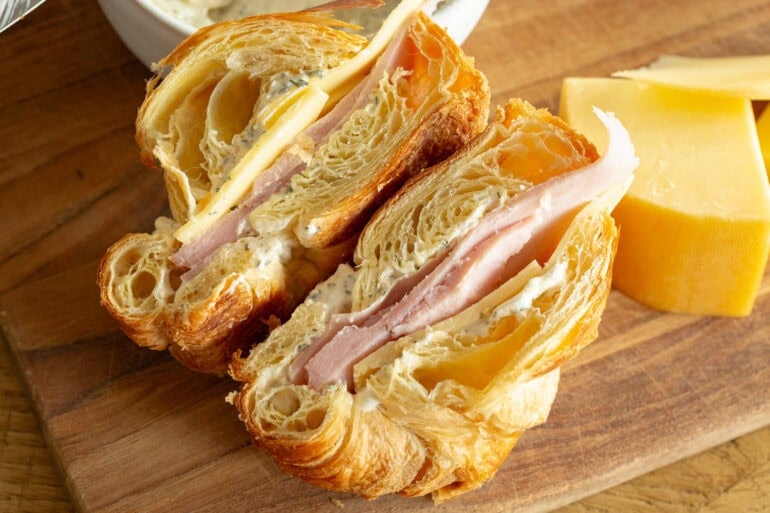 a ham and cheese sandwich on a flaky croissant that has been sliced in half so you can see the inside of each half