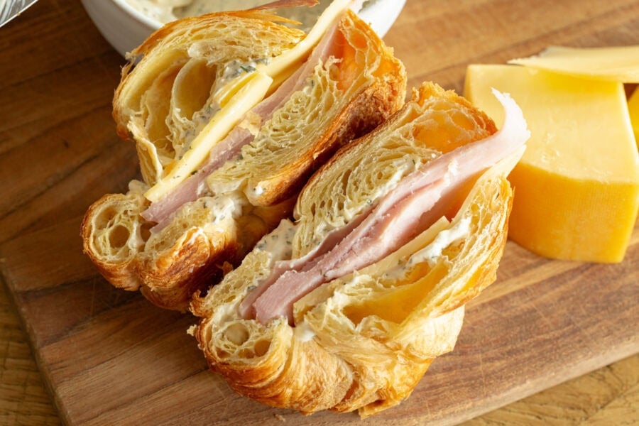 a ham and cheese sandwich on a flaky croissant that has been sliced in half so you can see the inside of each half
