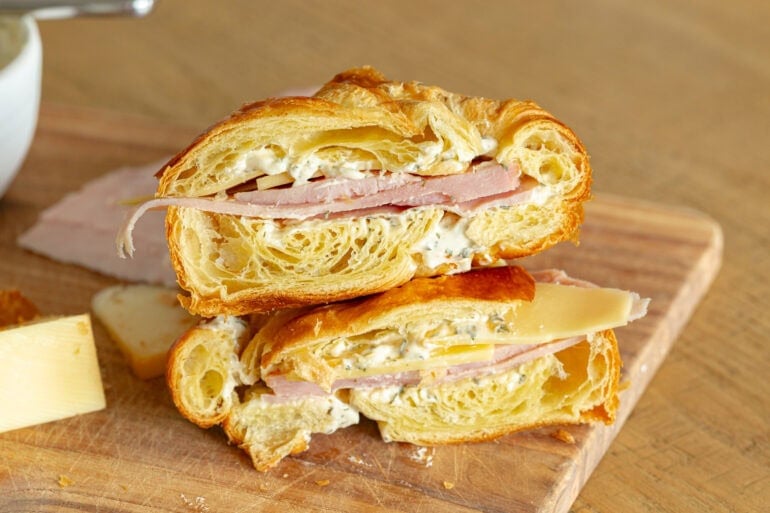a ham and cheese sandwich on a croissant with a garlic spread that has been cut in half with the two halves stacked on each other