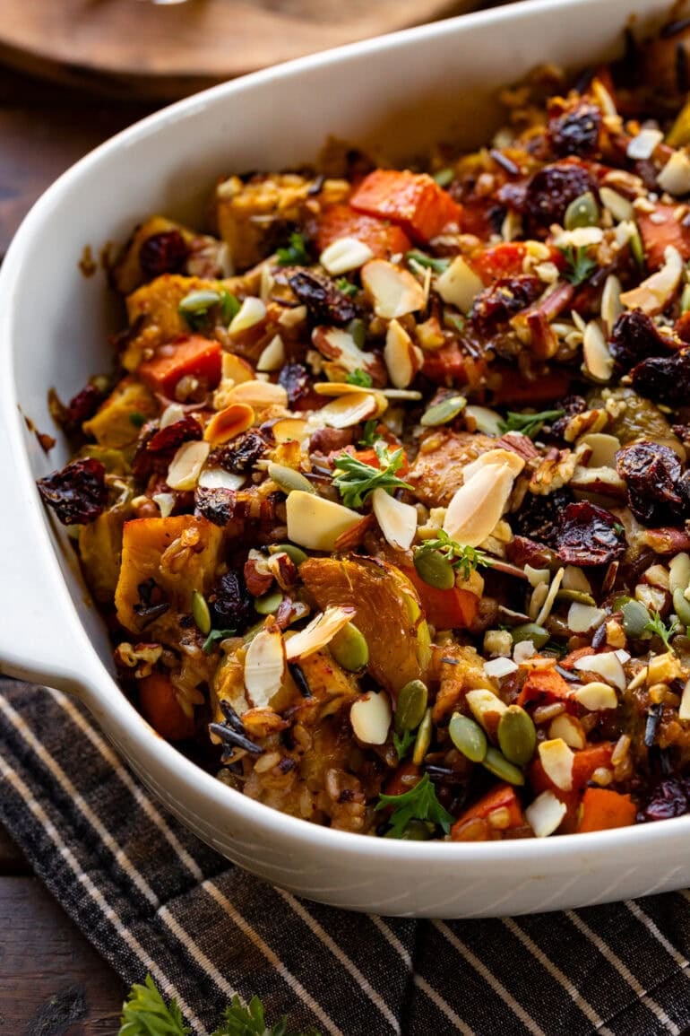 a photo of a white baking dish full of harvest chicken casserole including chicken, sweet potatoes, brussels sprouts, pepitas, red onion in a creamy sauce