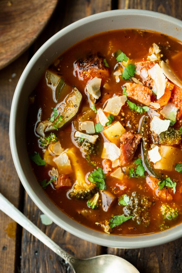 a photo of a bowl of hearty ham and vegetable soup loaded with potatoes, carrots, tomatoes, mushrooms and topped with chopped parsley