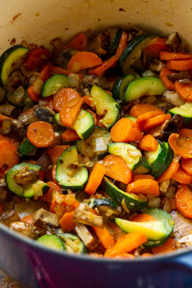 a photo of a zucchini, carrots, onions and mushrooms being sauteed in a dutch oven