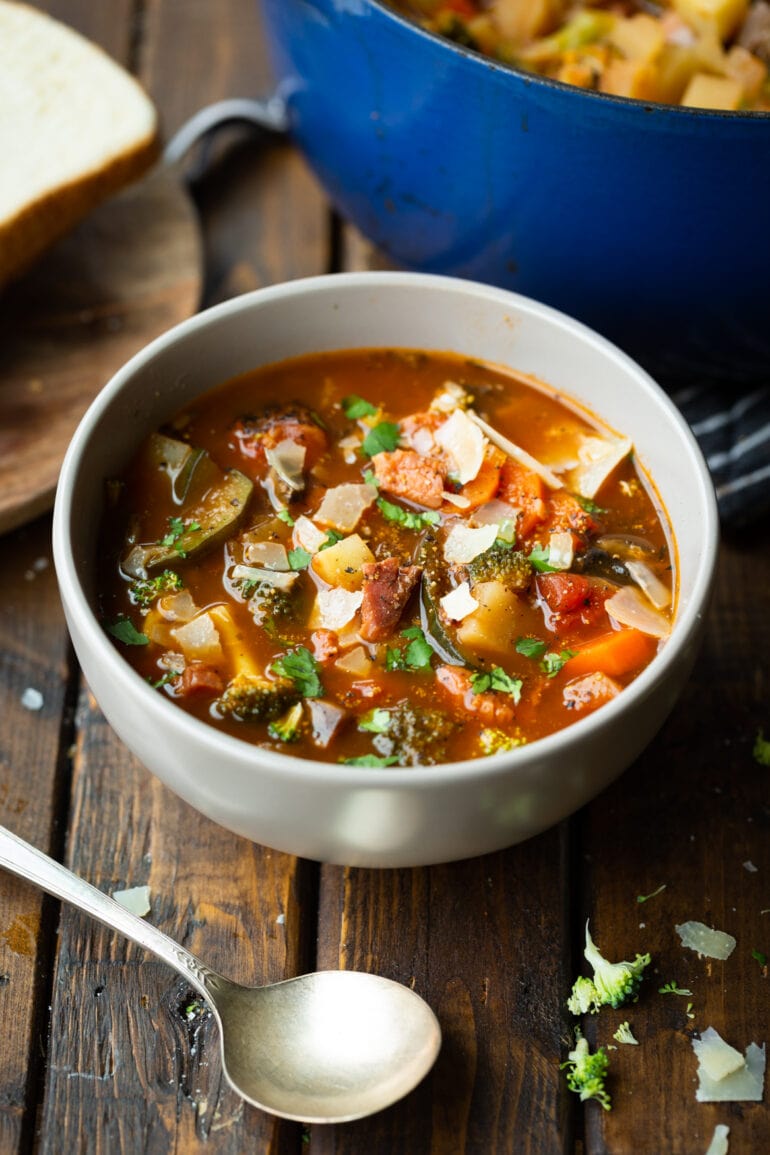 a photo of a bowl of hearty ham and vegetable soup sitting on a wooden table