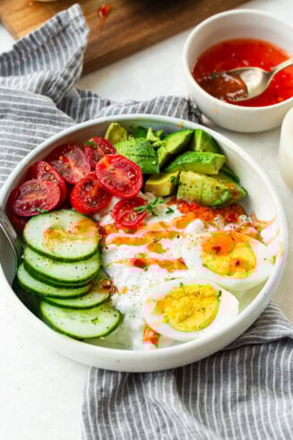 a photo of a large bowl full of cottage cheese, hard boiled eggs, sliced cucumber, cherry tomatoes and avocado topped with sweet chili sauce