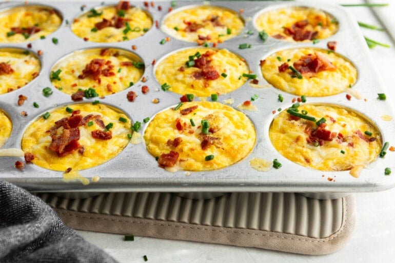 A muffin tin filled with savory eggy muffins topped with bacon and chives