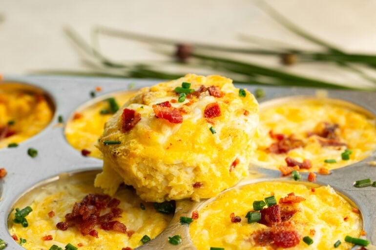 A muffin tin with cottage cheese egg bites garnished with bacon and chives