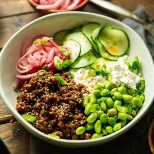 a photo of a bowl full of saucy korean ground beef with cottage cheese, edamame, pickled onions and thin slices of cucumbers