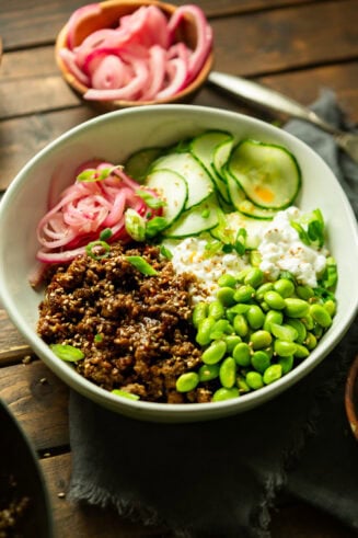 a photo of a bowl full of saucy korean ground beef with cottage cheese, edamame, pickled onions and thin slices of cucumbers