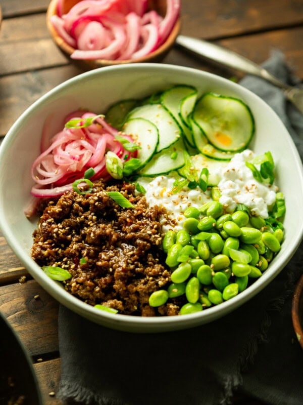 a photo of a bowl full of saucy korean ground beef with cottage cheese, edamame, pickled onions and thin slices of cucumbers