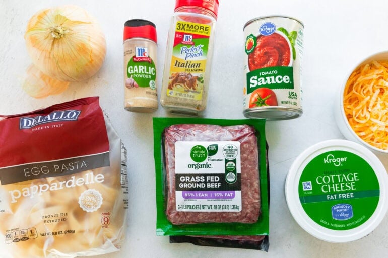 all the ingredients for creamy beef noodle casserole including ground beef, tomato sauce, garlic powder, oniones, cottage cheese and shredded cheese