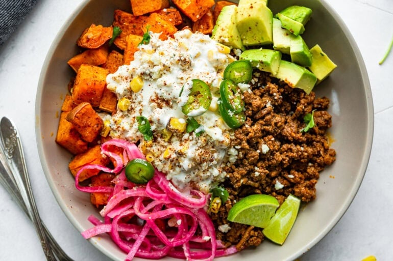 a mexican street corn sweet potato bowl with ground beef, avocado, pickled red onions and lime