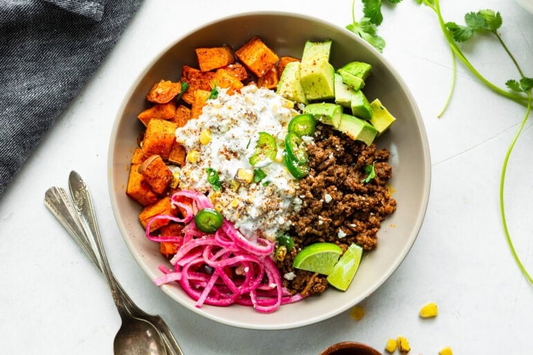 a ground beef sweet potato bowl with elote street corn, avocado chunks and picked red onions