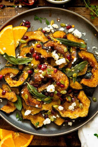 a photo of slices of roasted acorn squash topped with pomegranate seeds, feta, fried fresh sage, and fresh thyme.