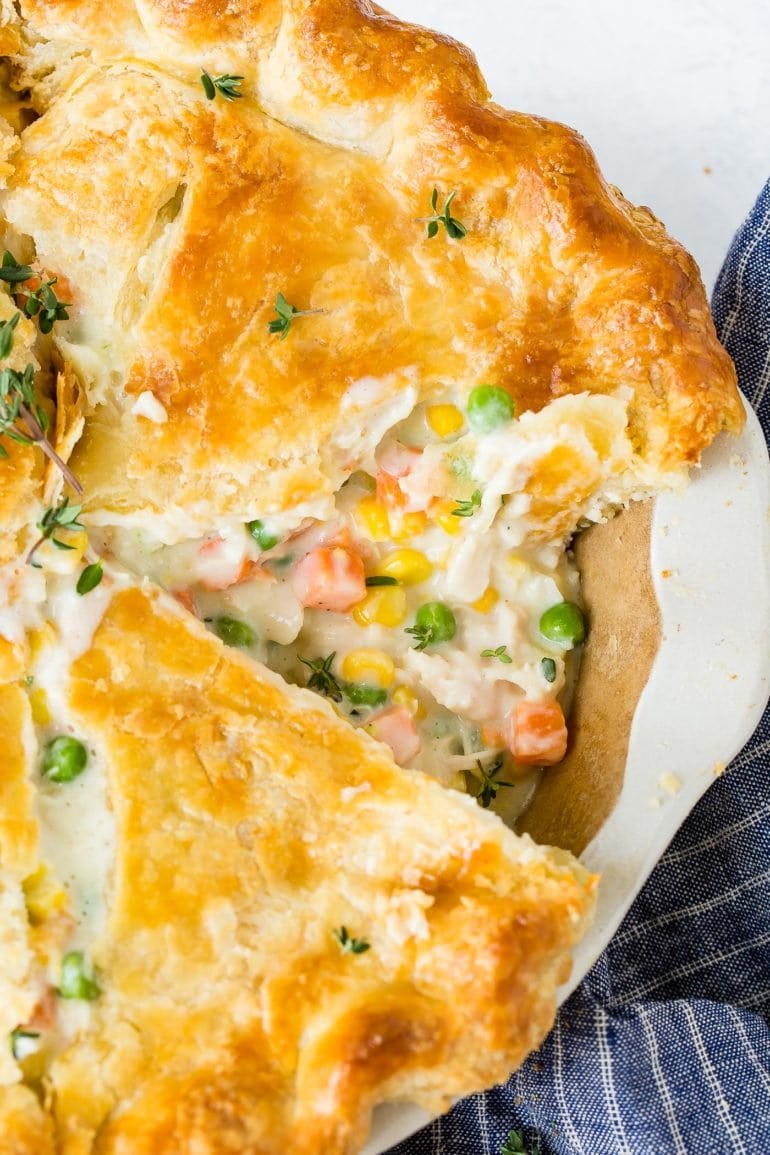 A whole chicken pot pie with one piece cut showing the creamy sauce and carrots and peas and chicken in the filling.